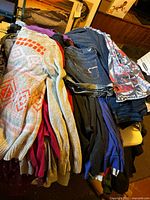 Various casual clothing items including sweaters, denim jeans, jean shorts, and casual tops piled on a table.