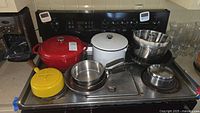 Wide view of stove with cookware including red Lodge cast iron Dutch oven, yellow Dansk enamel pot with lid, stainless steel pots and pans, metal bundt pans, and partial glassware