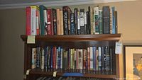 Two wooden shelves filled with approximately 50 hardcover books of various genres and colors.