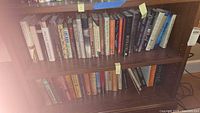 View of two wooden shelves filled with hardcover books, showing the spines and titles on multiple books.