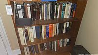 First photo shows three shelves of hardcover books, mostly history and political subjects with a black speaker and clock radio on the top shelf.