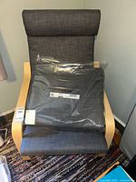 IKEA Poäng chair with extra cushion in plastic packaging displayed on chair seat.