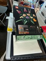 Photo showing LEGO Botanical Collection Flower Bouquet box on top of several sketch pads and white boards, arranged in a pile.