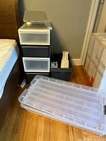 Photo showing 4 stacking plastic drawer cabinets in black and white with varying drawer sizes and a large clear plastic underbed storage bin with lid on floor nearby.