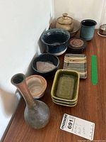Overview of pottery lot showing bowls, vase, coasters, and lidded jar on wood surface.