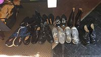 Wide shot of 6 pairs of shoes on floor, various styles and colors including black, brown, grey and navy