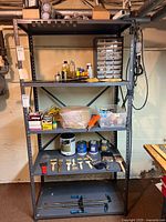 Full view of five-shelf metal storage unit with various tools, hardware containers, paint cans, brushes, clamps, hand saws, and other items arranged on shelves.