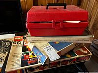 Closed red plastic Erector carrying case placed on top of two vintage Lego boxes and manuals laid flat on a table.