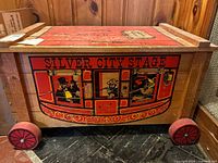 Front view of wooden toy chest showing Silver City Stage painted stagecoach scene and red wheels.