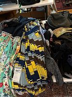 Photo showing a pile of mixed patterned skirts and tops, colorful, including floral and geometric prints, with some accessories visible.