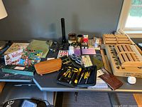 View of wooden box, drafting tools, flashlight, goggles, puzzle, papers, wallets, and other small items on a table