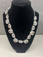 Front view of the necklace displayed on a black velvet bust showing clear oval and round crystal stones linked together.