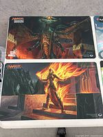 Two play mats with Magic the Gathering logos and fantasy creatures including armored dragon and fiery warrior on table