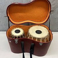 Opened hard case showing tabla set inside, with orange lining and two drums side by side.