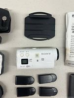 Top down view of Sony Action Cam Mini HDR-AZ1VR with mounting plate, USB caps, battery, and instruction manual.