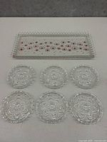 Rectangular glass tray with beaded edge and red flower dot pattern, six matching round coasters with floral design and beaded rims displayed on table