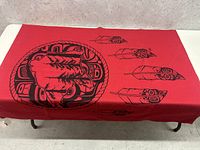 Top view of the red blanket showing circular Great Bear Rainforest design with trees and animal motifs and four feathers.