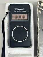 Micro cassette tape recorder close-up showing device with cassette inside and speaker grill.