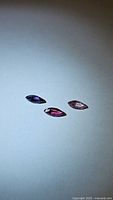 Photo of three marquis cut sapphires of varying purple, pink, and violet hues displayed on a light background