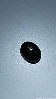 Photo of 1.84ct natural oval cabochon black star diopside gemstone showing star asterism on glossy black surface.