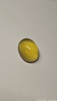 Oval lemon citrine cabochon gemstone on white background showing smooth polished surface and deep lemon-yellow color with reflective highlight.