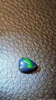 Close-up of pear-shaped Ethiopian black opal cabochon showing blue body tone with vivid green and orange play-of-color.