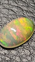 Close-up photo of natural Ethiopian opal showing rainbow color flashes on black surface.