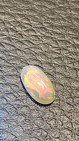 Oval cabochon-shaped natural Ethiopian opal gemstone on black textured surface showing bright rainbow flashes under light.