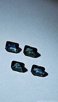 Four natural blue sapphires, emerald cut, arranged on a plain background, showing facets and color under direct light.