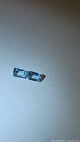 Pair of natural blue topaz stones on a white background showing emerald cut and clear blue color