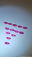 14 natural heated Burma rubies laid out on a white background showing marquis cut and pinkish-red color.