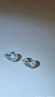 Pair of pear cut colorless gemstones on white background showing clarity and facets.
