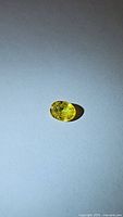 Close-up image of bright yellow oval cut sapphire gemstone with some visible internal inclusions, lying on a white surface under bright lighting.