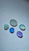 Five natural chalcedony cabochon gemstones displayed on a white background, showcasing mixed colors and shapes.