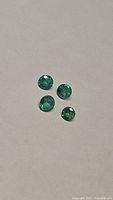Four natural round cut emerald gemstones arranged on a neutral background under normal light, showing their clarity and green color.