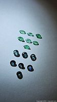 Photo showing 7 marquise-cut natural emerald gemstones and 8 round blue-green sapphire gemstones.