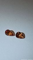 Pair of pear-shaped Fanta orange sapphires placed on a light surface, showing their faceted cut and color.
