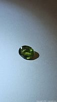 Close-up of a single oval cut natural green sapphire gemstone on a plain surface showing its rich green color and facets.