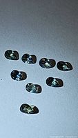 Nine pear cut green sapphires arranged on a white surface, showing their color, size, and clarity.