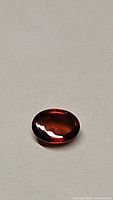 Oval cabochon cut natural burnt orange hessonite garnet gemstone shown on a plain surface with light reflections.