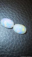 Close-up photo of two oval natural Ethiopian opal cabochons showing their color play on a black textured surface.