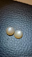Photo of two round peach moonstones on a textured dark surface, showing their translucent coruscating qualities and polished cabochon shape.
