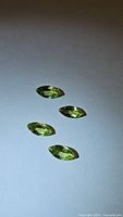 Four marquis cut yellow-green peridot gemstones on white background with good lighting showing facets and clarity.