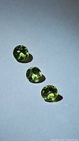 Three round natural peridot gemstones placed in a line on a white surface, showing clear apple green color and faceted cuts.
