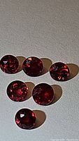 Top view of six round faceted deep red rubies showing clarity and color under lighting.