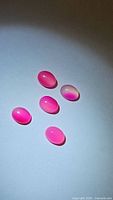 Five natural bright pink chalcedony oval cabochons arranged on a white background with subtle shadows, showing translucent pink color and smooth polished surfaces.