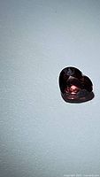 Close-up photo of single heart-shaped purple pink zircon gemstone on white background.
