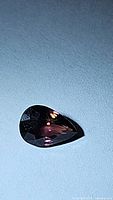 Pear shaped sapphire showing dark purple color on light blue background.