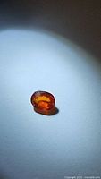 Deep orange untreated natural sapphire placed on a white background showing the gemstone's color, clarity and polished oval cut.