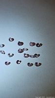 Multiple loose pastel colored spinel gemstones from Myanmar with diamond cut, about 2.5mm in size each, arranged on a light surface in natural lighting with flash causing slight reflections.
